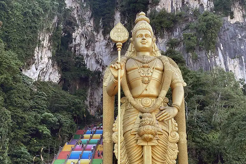 The Ultimate Guide To The 10 Best Day Trips from Kuala Lumpur (Local Expert Edition) 10 The golden Lord Murugan statue at Batu Caves with the colourful staircase and limestone cliffs behind it.