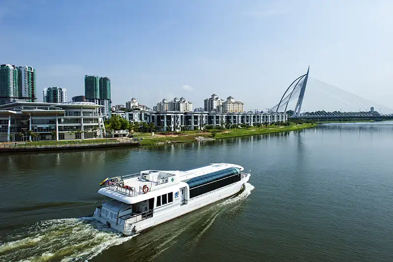 The Ultimate Guide To The 10 Best Day Trips from Kuala Lumpur (Local Expert Edition) 6 A sightseeing boat cruising along the lake in Putrajaya with modern buildings and a cable-stayed bridge in the background.